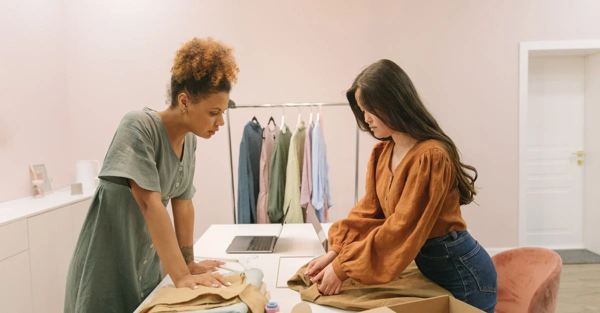 Deux jeunes femmes travaillant ensemble dans une boutique moderne, organisant des vêtements avec concentration et style.