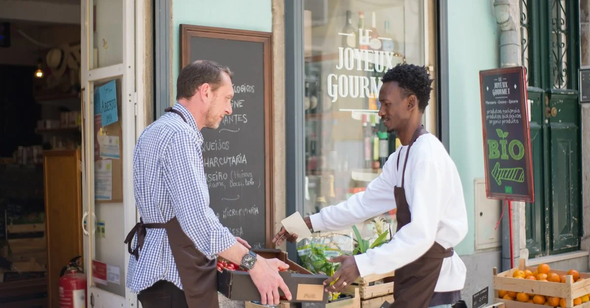 Deux hommes arrangeant des fruits et légumes devant un magasin au Portugal.
