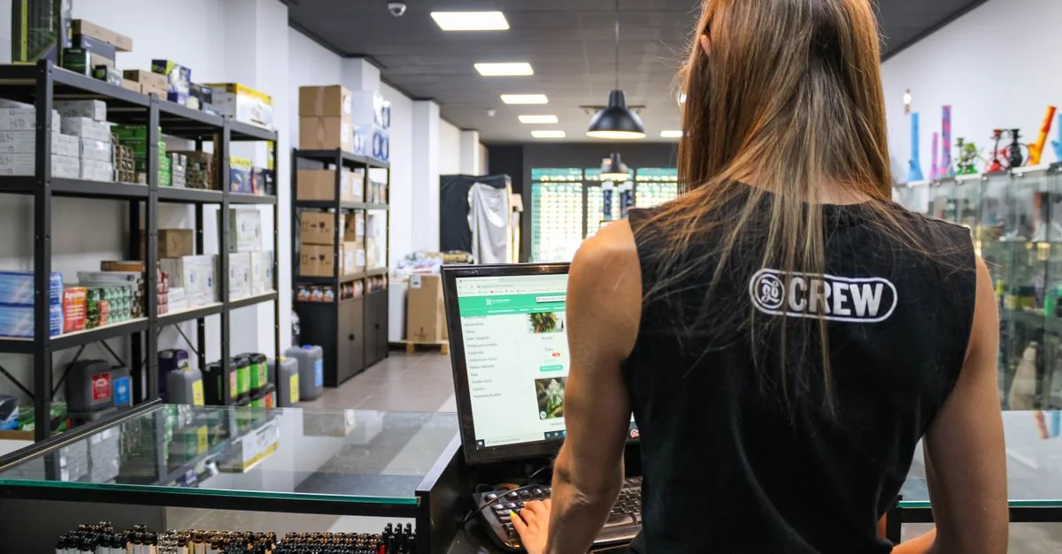 Un vendeur interagit avec un ordinateur au comptoir d'un magasin rempli de marchandises diverses.