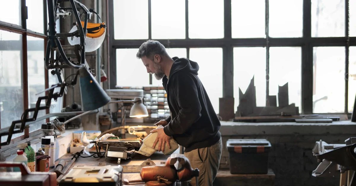 Un artisan expérimenté se concentrant sur son travail dans un atelier en désordre avec divers outils et machines.