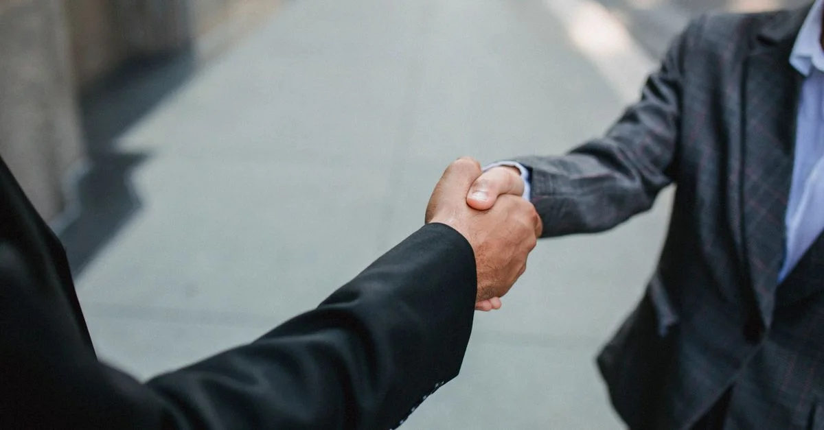 Gros plan de deux hommes d'affaires se serrant la main à l'extérieur, symbolisant le partenariat et l'accord.